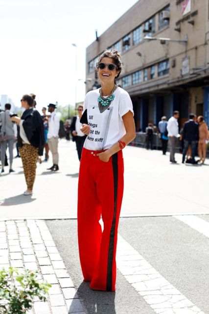 a trendy look with a printed tee, red side-striped pants, statement necklaces and a clutch bag