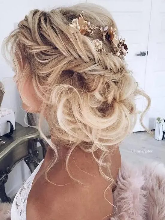 a braided messy updo with some locks down and some curls around the face plus a flower hairpiece will be great for boho brides