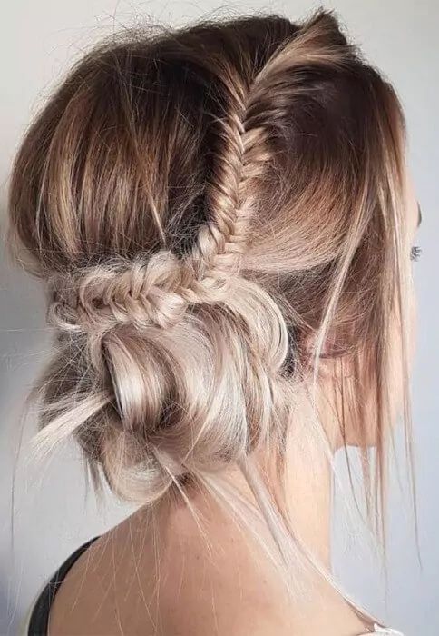 a messy updo with a side fishtail braid and a low bun plus a bump on top is a cool and catchy idea