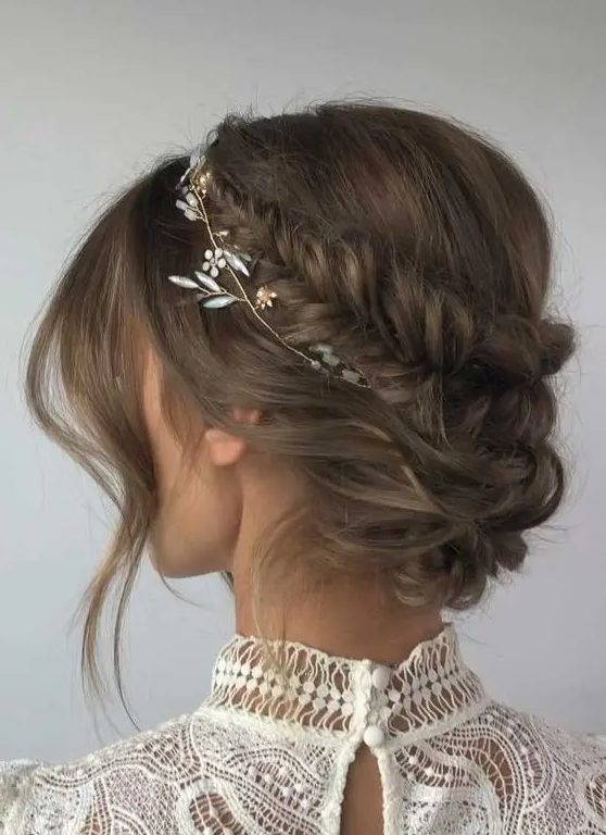 an updo with a fishtail braided halo, a low bun and face-framing locks plus a hair vine accenting the hairstyle