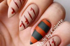 matte nude nails with bleeding scratches, a striped black and orange accent nail for Halloween
