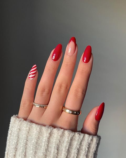 a classic red Christmas manicure with a nude and tip nail and a candy cane one is a lovely and bright idea
