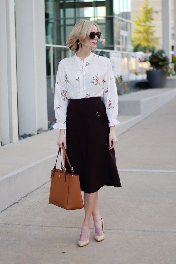 a fall work outfit with a floral blouse, a black A-line midi, nude shoes and a rust-colored bag