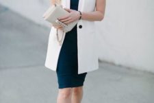a navy knee fitting dress with no sleeves and a high neckline, a long sleeveless blazer and white shoes plus a neutral clutch