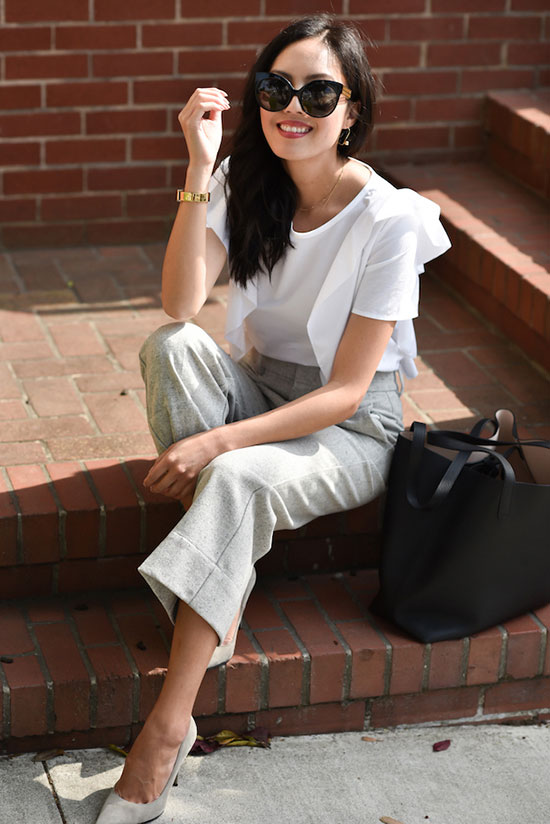 a white blouse with ruffle sleeves, grey cropped pants, grey shoes and a black tote for a monochromatic look