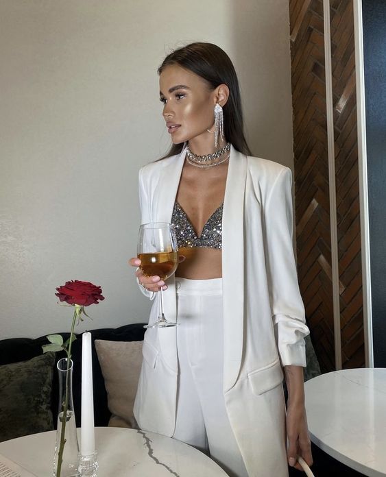 a white pantsuit with an oversized blazer, a silver sequin bra, statement jewelry are a luxurious outfit for NYE