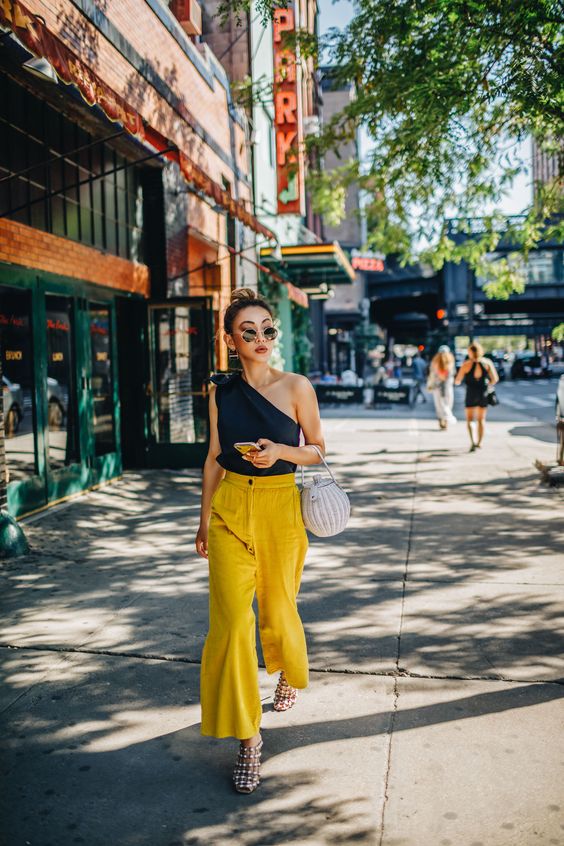 a black one shoulder top, sunny yellow pants, shiny shoes and a white basket bag for summer