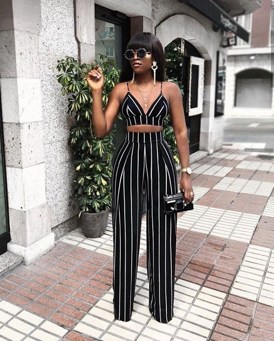 a black striped crop top and high waisted palazzo pants, white statement earrings and layered necklaces