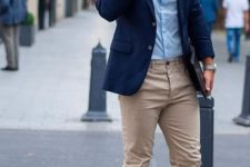 a casual work outfit with a blue button up, a navy jacket, tan chinos, white sneakers