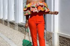 a colorful floral off the shoulder ruffle top, orange high waisted pants, acrylic heels and a green bag