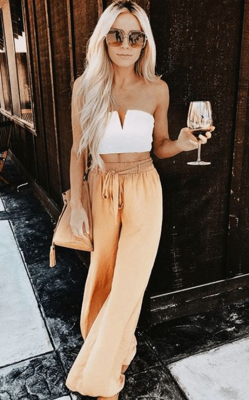 a white crop top with a cut, chic rust-colored palazzo pants, a matching bag and large sunglasses
