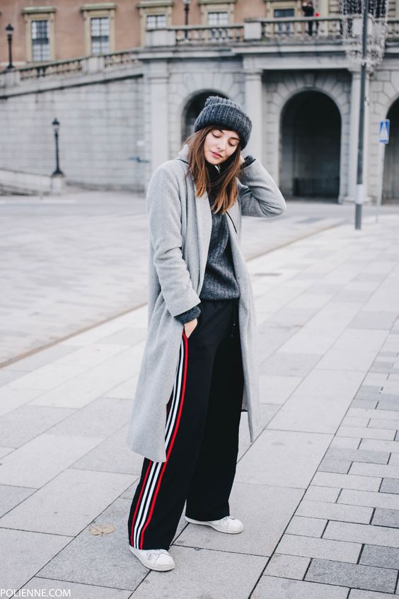 a winter outfit with a grey sweater, black side stripe pants, white sneakers, a grey beanie and a grey coat