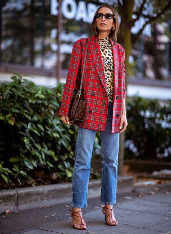 a bright Christmas look with a leopard print turtleneck, blue jeans, red strappy heels, a bold red plaid blazer and a brown bag