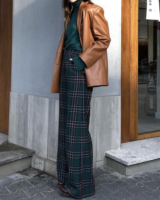 a stylish Christmas look with a green turtleneck, green and navy pants, a camel elather jacket