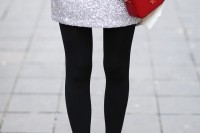 an oversized white sweater, a silver sequin mini skirt, black tights, black shoes, a red bag and a watch plus bracelets
