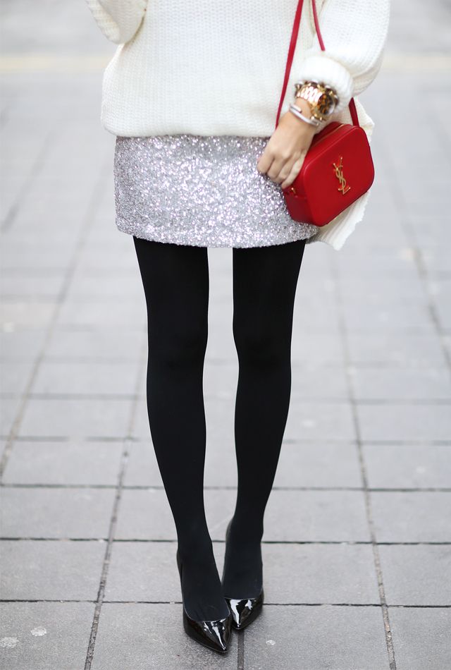an oversized white sweater, a silver sequin mini skirt, black tights, black shoes, a red bag and a watch plus bracelets