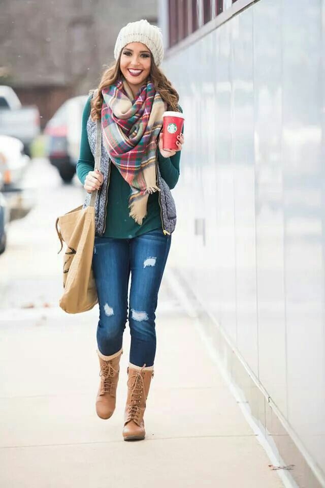a relaxed Christmas outfit with a grene top and blue ripped jeans, camel boots and neutral socks, a quilted vest and a plaid scarf, a neutral canvas tote and a beanie