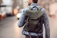 a green backpack with dark brown leather detailing is a cool piece that will match many looks with its muted color