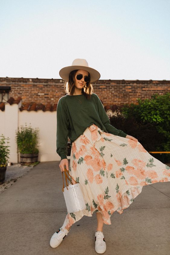 a green oversized top, a bright floral print midi skirt, white sneakers, a bucket bag and a hat