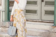 a statement print outfit with a white top, a yellow floral layered maxi skirt, white cowboy boots, a grey tote and a hat