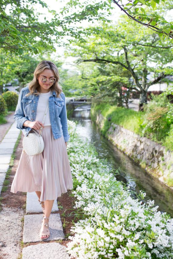 a white tee, a blush pleated midi, blush strappy shoes, a white round bag and a blue denim jacket