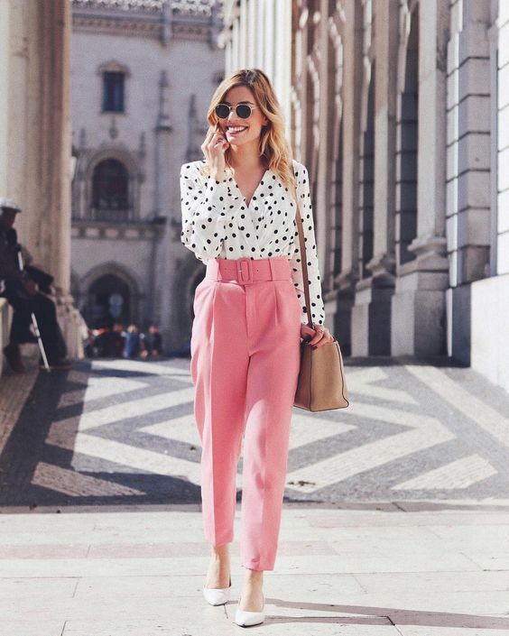 a bright spring work outfit with a white polka dot shirt, pink pants, white shoes and a tan bag to rock