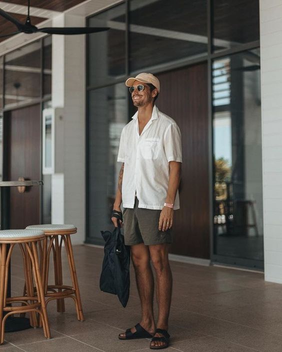 a white oversized short sleeve shirt, grey shorts, slippets and a cap for a hot summer day