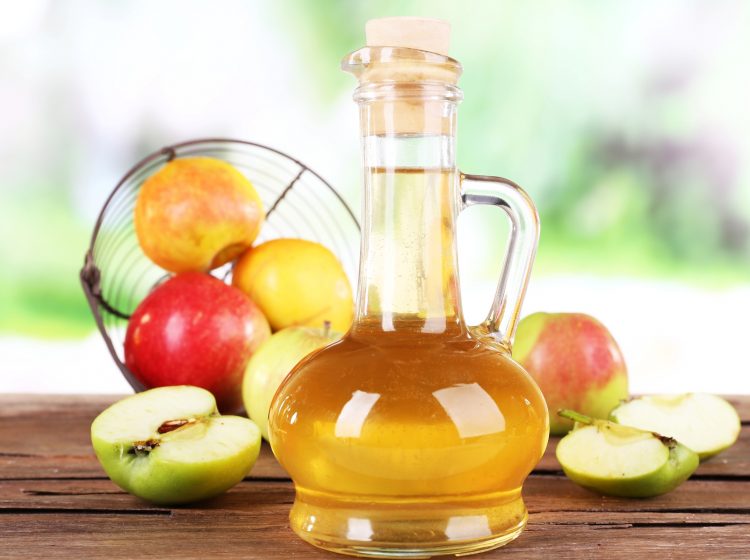 Apple cider vinegar in glass bottle and ripe fresh apples, on wooden table, on nature background