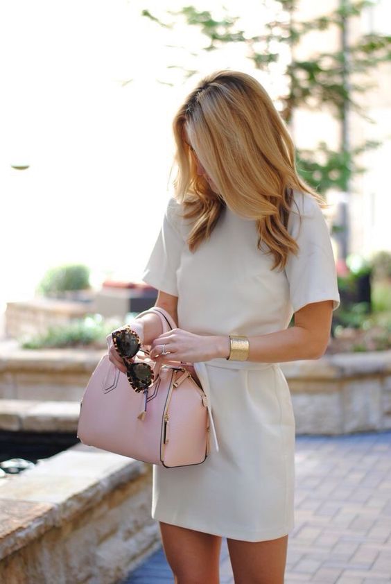 an off white mini dress with a pink purse and gold accessories
