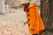 Orange coat with beige beanie, black pants and brown ankle boots