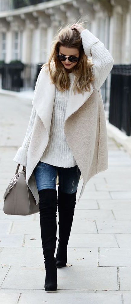 black knee-length boots, jeans, a white chunky knit sweater and a white coat