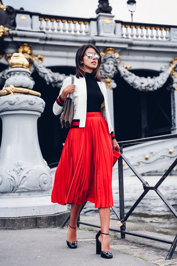 red pleated midi skirt, a black turtleneck, a white bomber jacket and heels