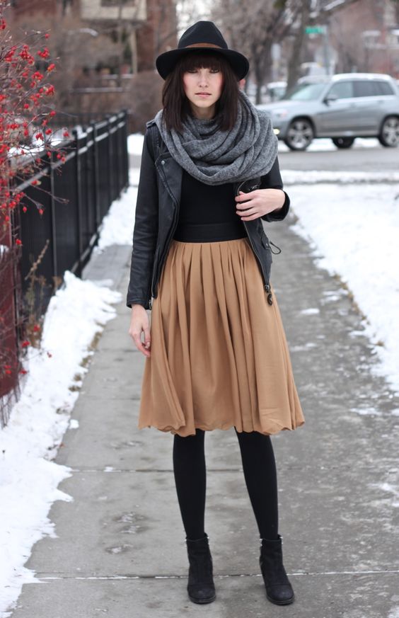 tan knee skirt, a black leather jacket and boots, a grey blanket scarf and a hat