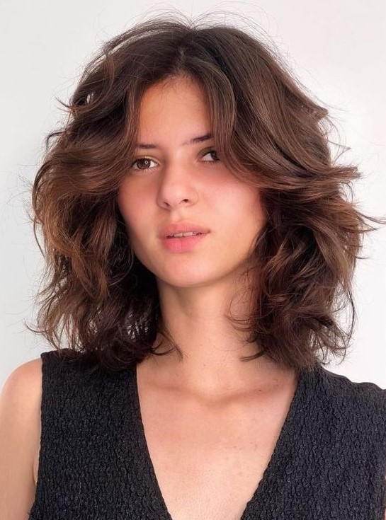A beautiful chestnut medium length butterfly haircut on wavy hair, with a lot of dimension