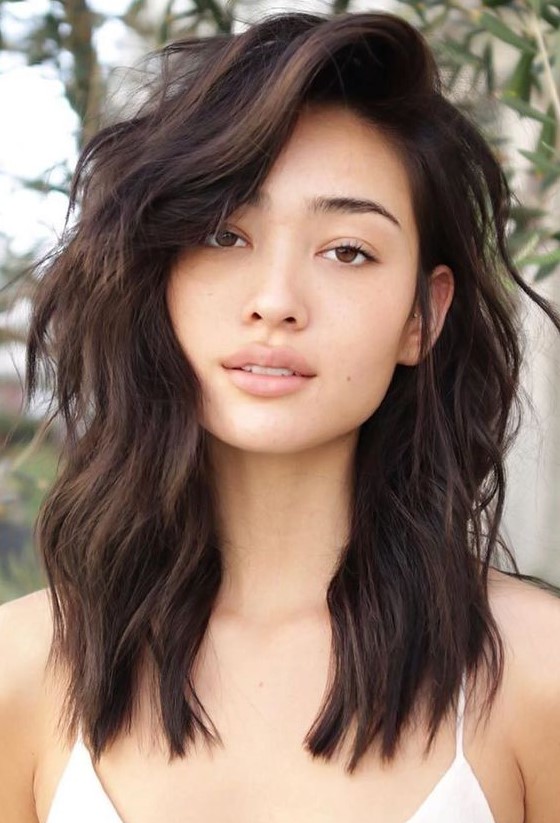 a dark chestnut medium haircut with a lot of volume, layers, side bangs and waves is a very chic idea
