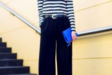 With striped shirt, black wide-leg trousers and clutch