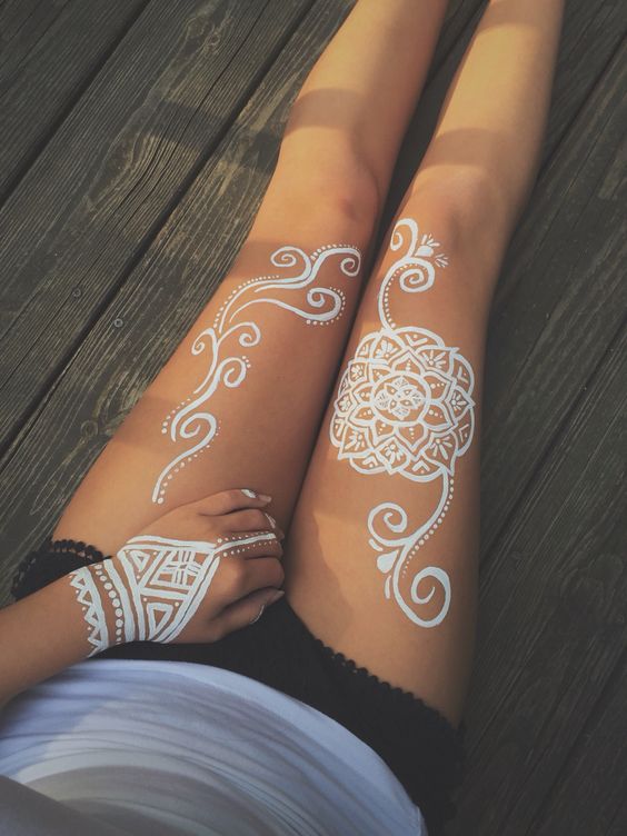 a white mandala on a hip, a pattern on the left one and a tattoo on the hand
