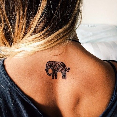 a small elephant tattoo on the upper part of the back