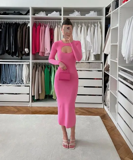 a pink bodycon midi dress with a cutout and long sleeves, white strappy shoes and a small pink bag