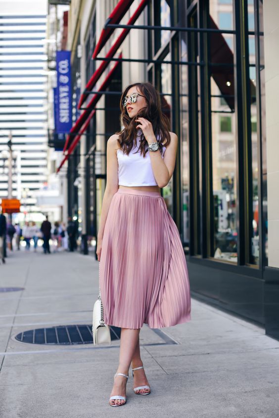a white halter neckline crop top and a pink pleated midi skirt, white heels and a bag