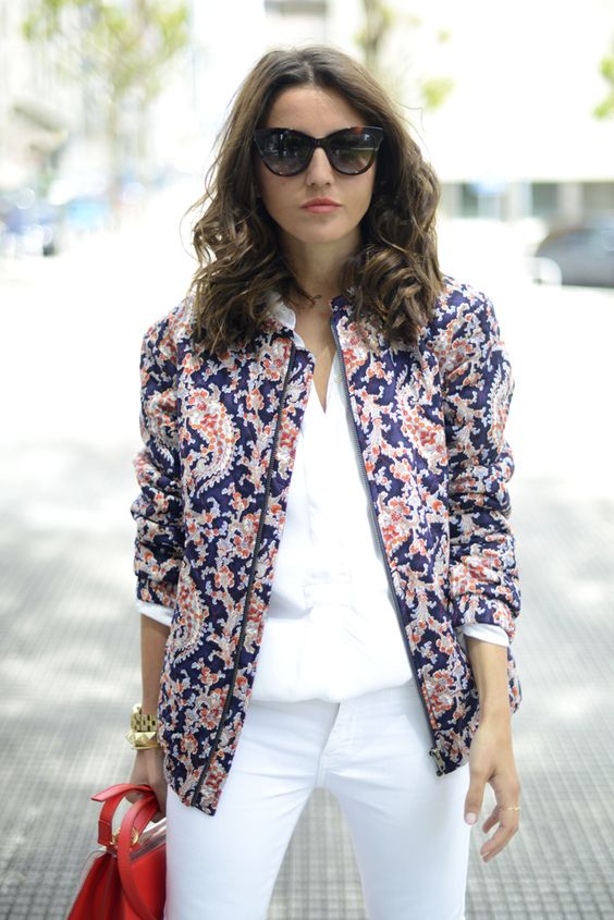 white pants, a white tee, a blue and red printed bomber jacket and a red bag