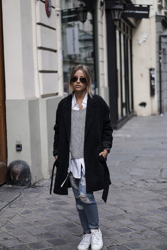 ripped jeans, a grey sweater, a white shirt, whit sneakers and a black coat