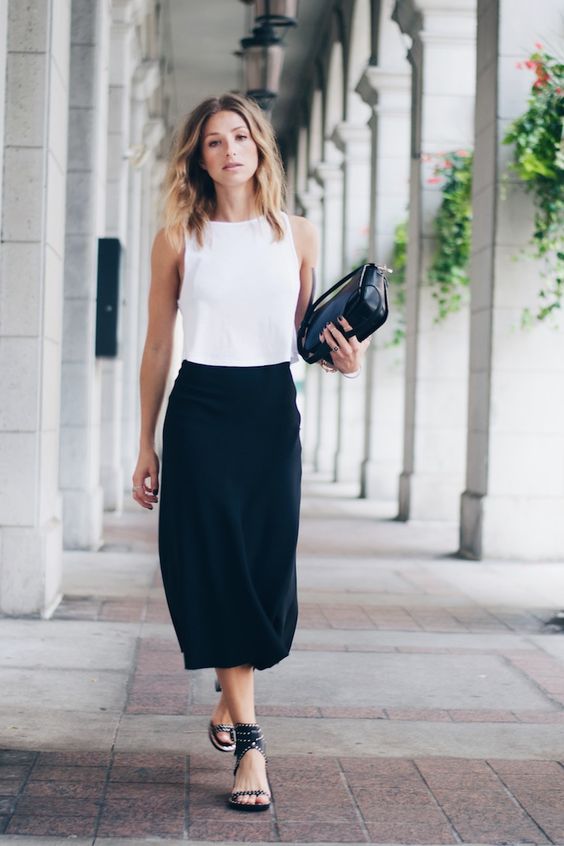 a black midi skirt, a white sleeveless crop top, black spiked shoes and a black bag