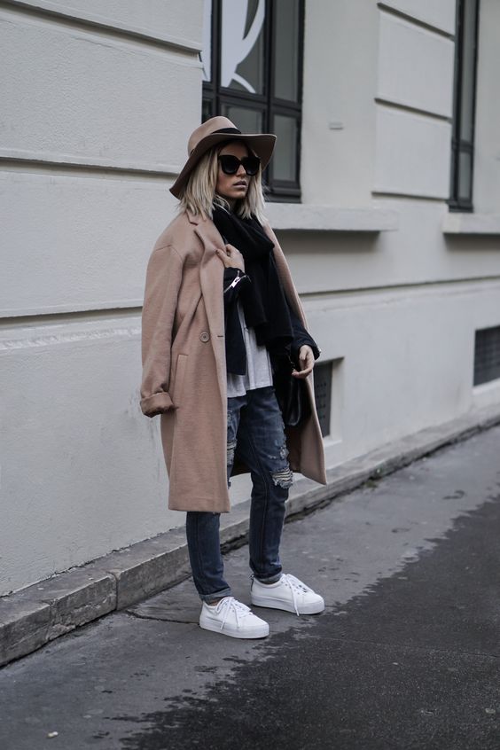 ripped jeans, white sneakers, a neutral top and a black scarf, a camel coat and a camel hat