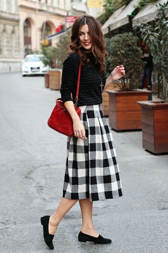 a striped black sweater, a plaid black and whiet skirt, black suede moccasins and a red bag