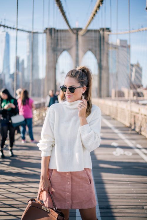 a white turtleneck slouchy sweater, a pink pocket mini skirt with a row of buttons and a brown bag