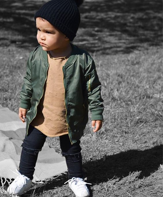 black ripped jeans, a tan shirt, an olive green jacket, white sneakers and a black beanie