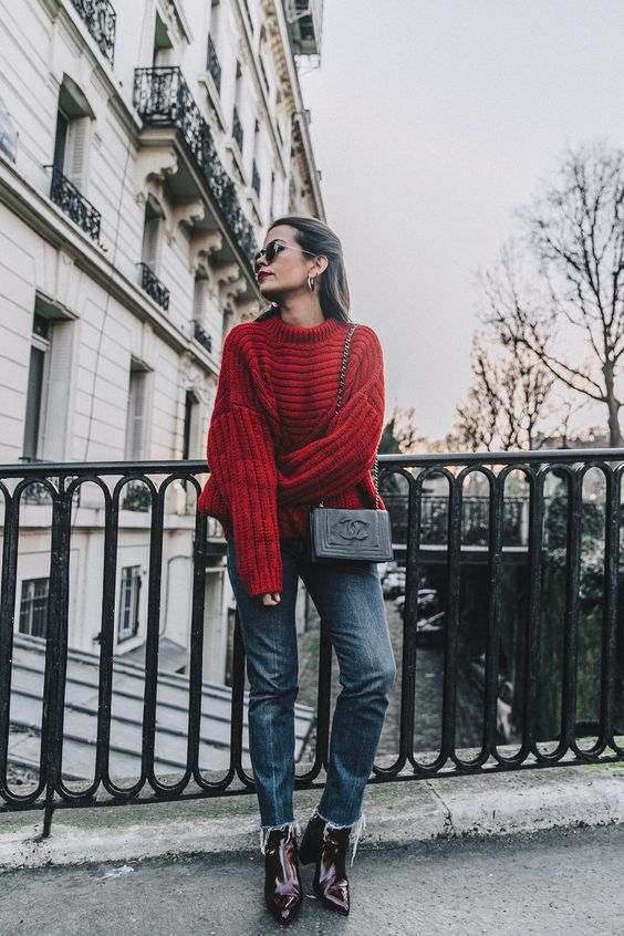 a red oversized sweater, blue jeans, burgundy boots and a Chanel bag
