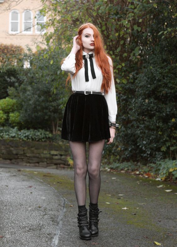 a white vintage-style shirt with a black bow and a brooch, a black velvet mini skirt, black tights and boots