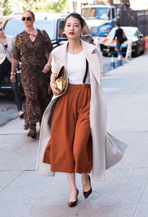 a white tee, burnt orange culottes, brown shoes, black suspenders and a creamy coat